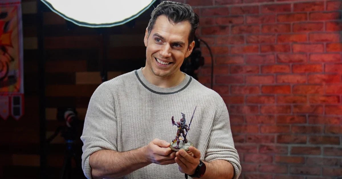 Smiling man holding a painted Warhammer miniature in a hobby studio