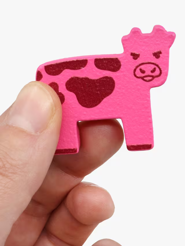 Close-up of the pink cow token from Herd Mentality travel held between fingers