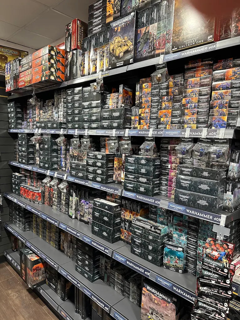 A retail store aisle filled with shelves stocked with boxed Warhammer 40k miniatures and accessories, including Space Marine, Warhammer 40k, and Warhammer 10k boxes.