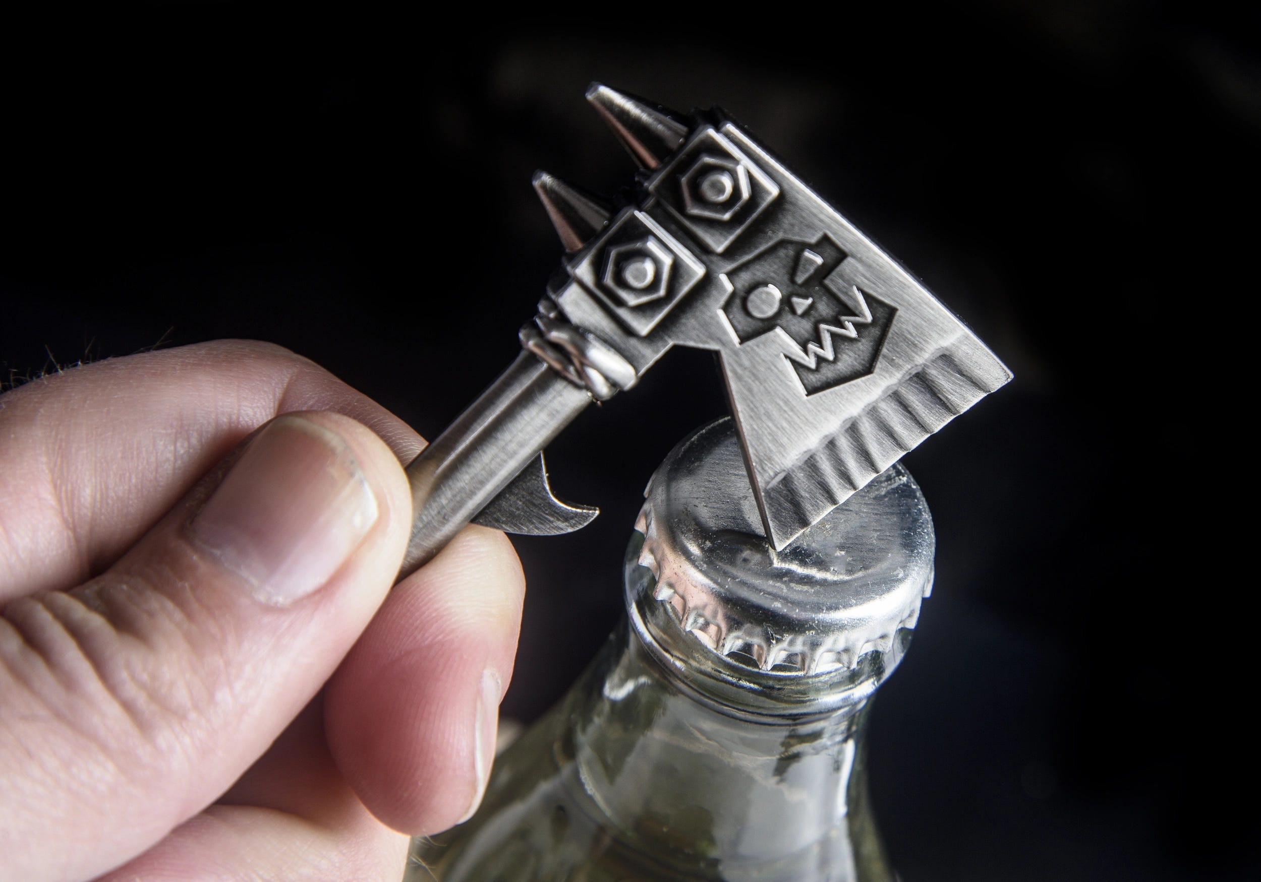 Hand using the Warhammer Ork choppa bottle opener to open a glass bottle