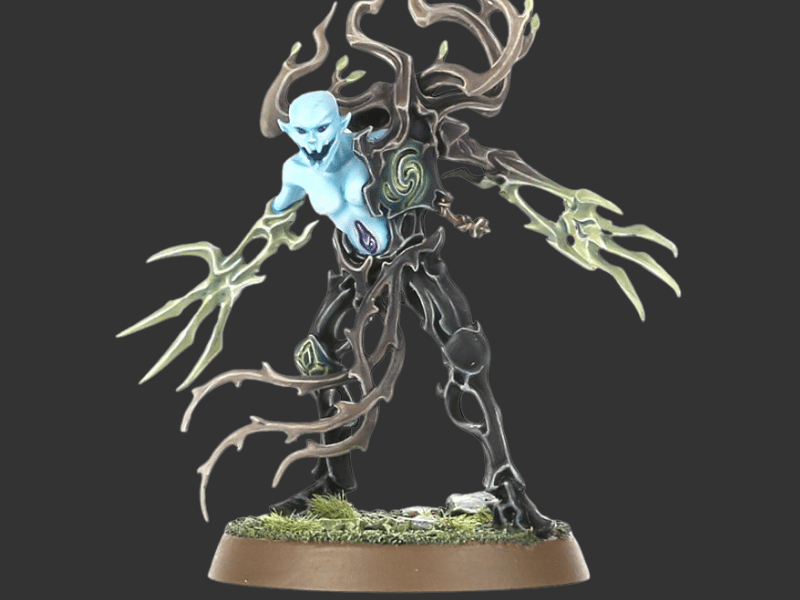 A painted fantasy miniature figurine of a pale blue-skinned entity with glowing green energy hands and dark tree-like limbs, standing on a round textured base against a dark gray background.