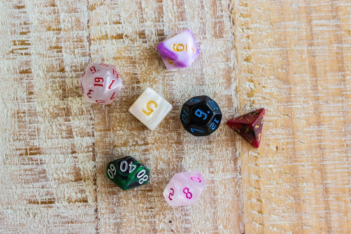Spread of seven mismatched Dice Goblin polyhedral dice on a light wood surface