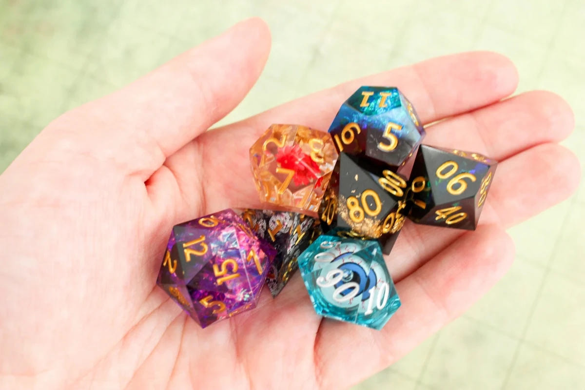 Handful of sharp-edged Dice Goblin polyhedral dice with swirling colours and gold numbers