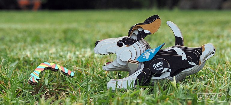 Built EUGY Hope cardboard dog playing on grass beside a toy