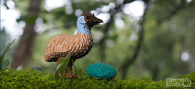 Finished EUGY Emu cardboard model standing on moss beside its teal egg, outdoor shot