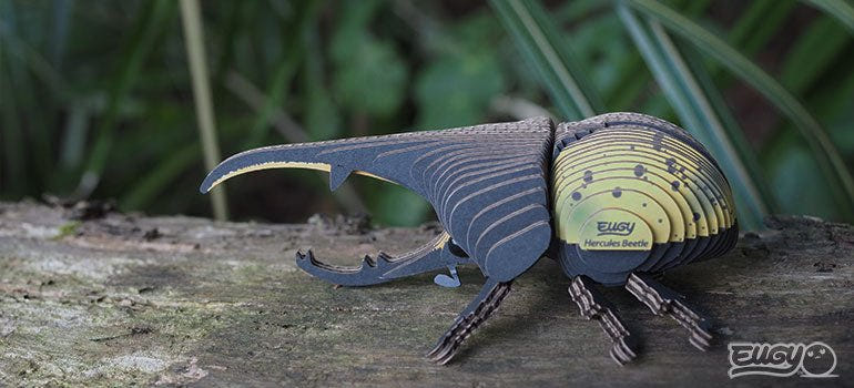 EUGY Hercules Beetle card model posed on a log in a garden setting