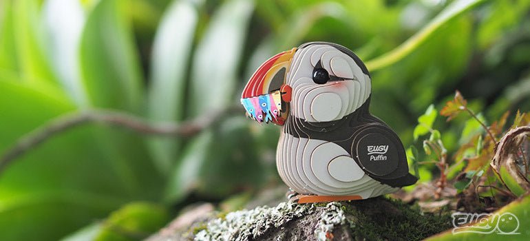 Finished EUGY Puffin card model perched on a mossy rock outdoors among green leaves