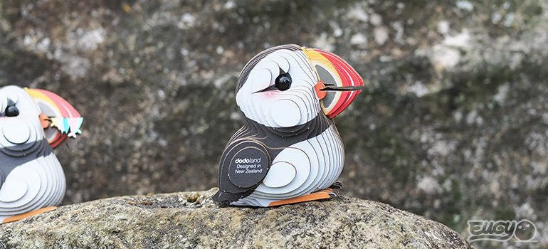 Two EUGY Puffin card models standing on a grey stone outdoors, side view