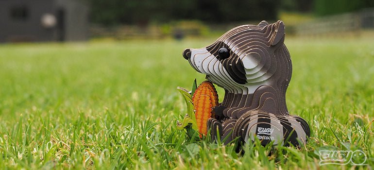 Finished EUGY Raccoon card model sitting on green grass outdoors, side view