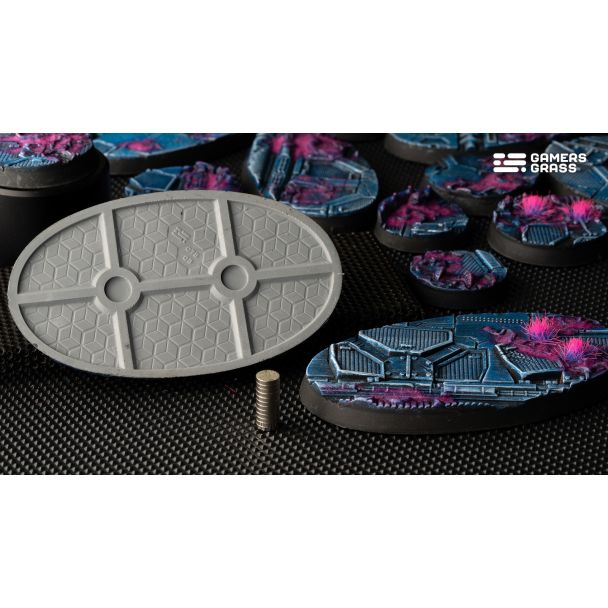 Grey underside of a Gamers Grass Alien Infestation oval base with magnet slots, beside painted bases