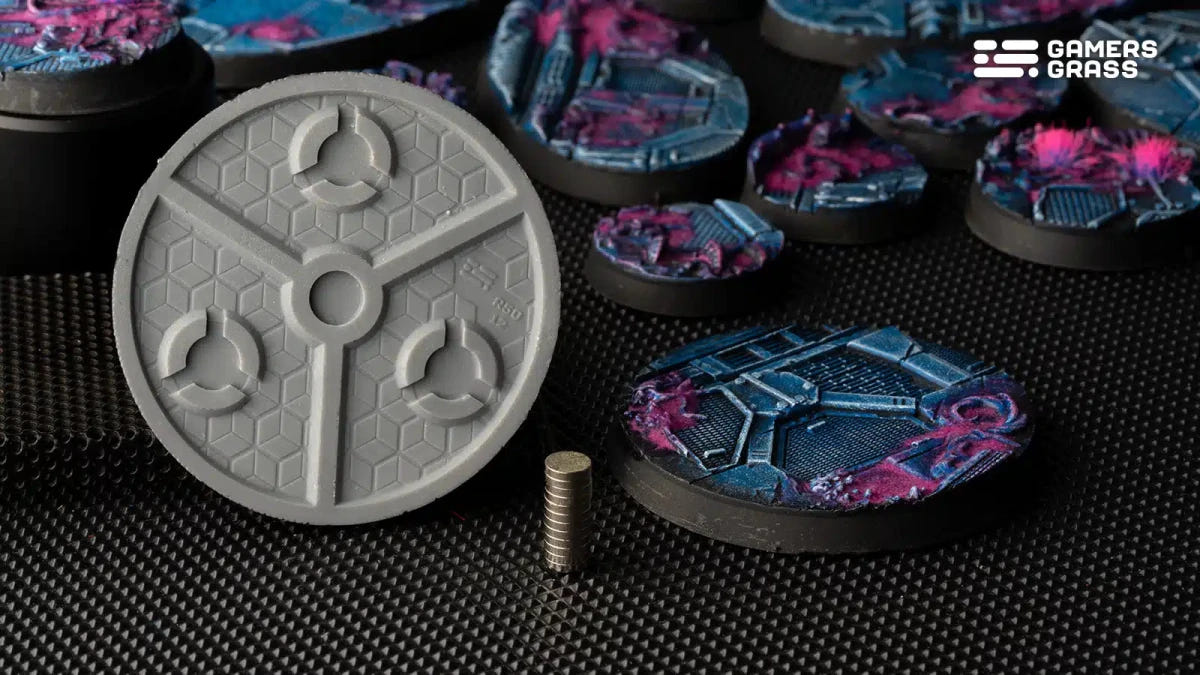 Grey underside of a Gamers Grass Alien Infestation round base with magnet slots, beside painted bases