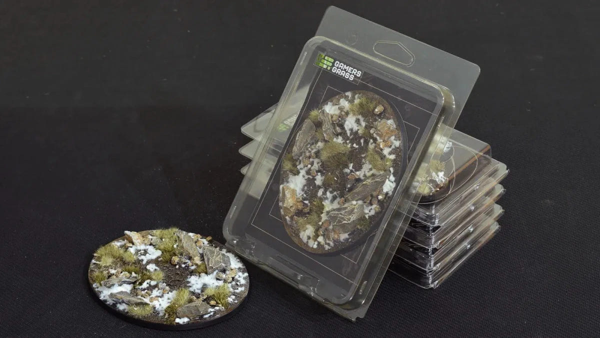Gamers Grass Battle Ready Winter 120mm oval base beside its blister pack, snowy rocky ground