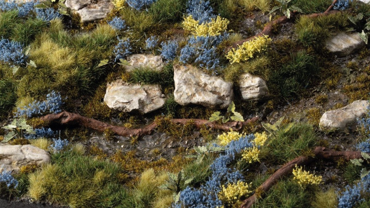 Rocky meadow diorama dotted with Gamers Grass Bluebeard Flowers blue tufts among green grass