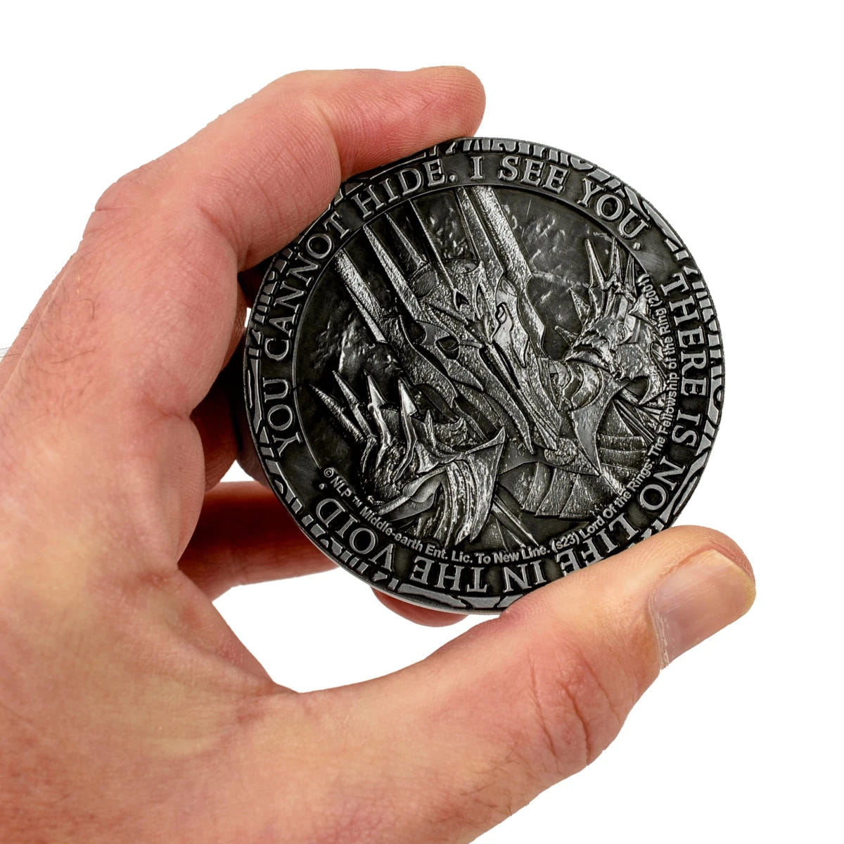 Hand holding the Sauron reverse of the coin with You Cannot Hide, I See You inscription