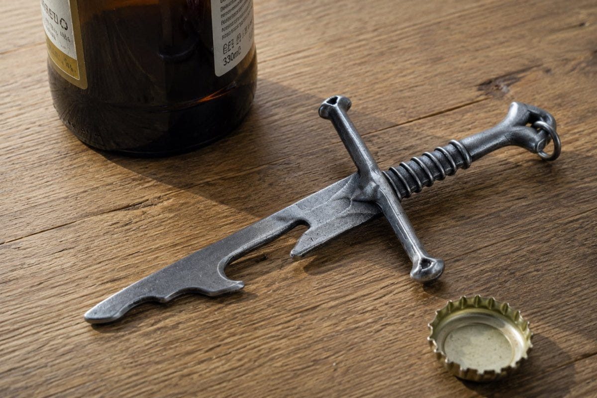 Narsil bottle opener on a wooden table beside a beer bottle and a bottle cap