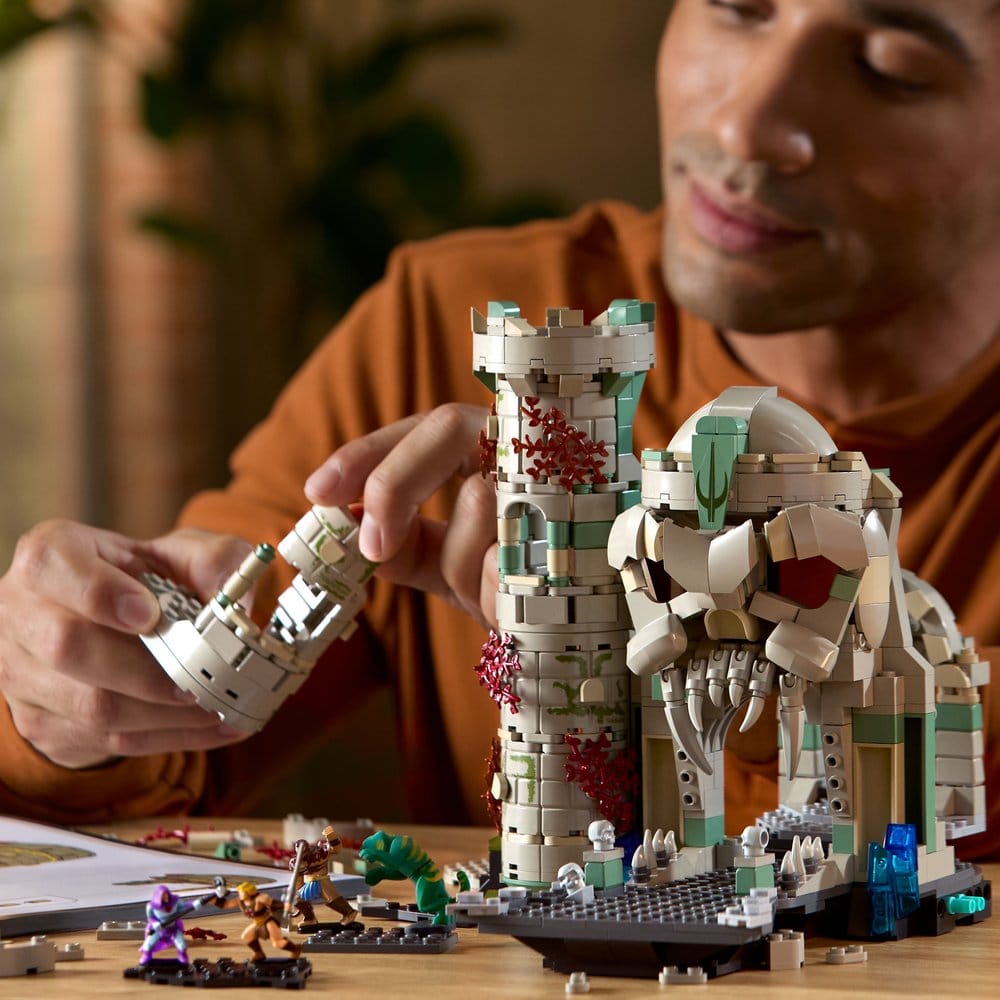 Adult building the Mattel Brick Shop Castle Grayskull set at a table, attaching a tower section