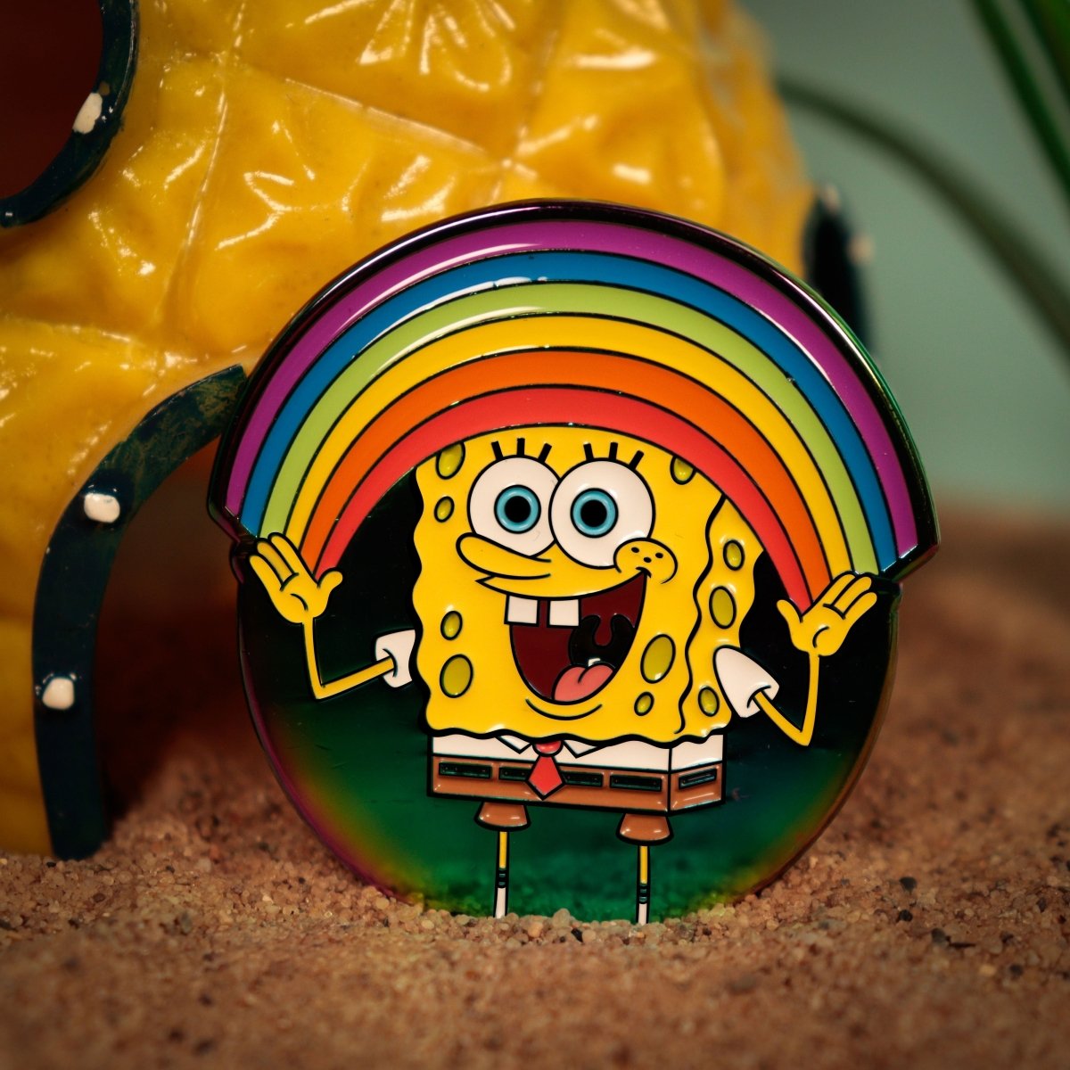 SpongeBob SquarePants rainbow pin badge propped up in front of a pineapple house prop