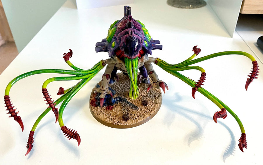 A finished Tyranid Toxicrene, painted in purple and acid green, on a sand-textured base