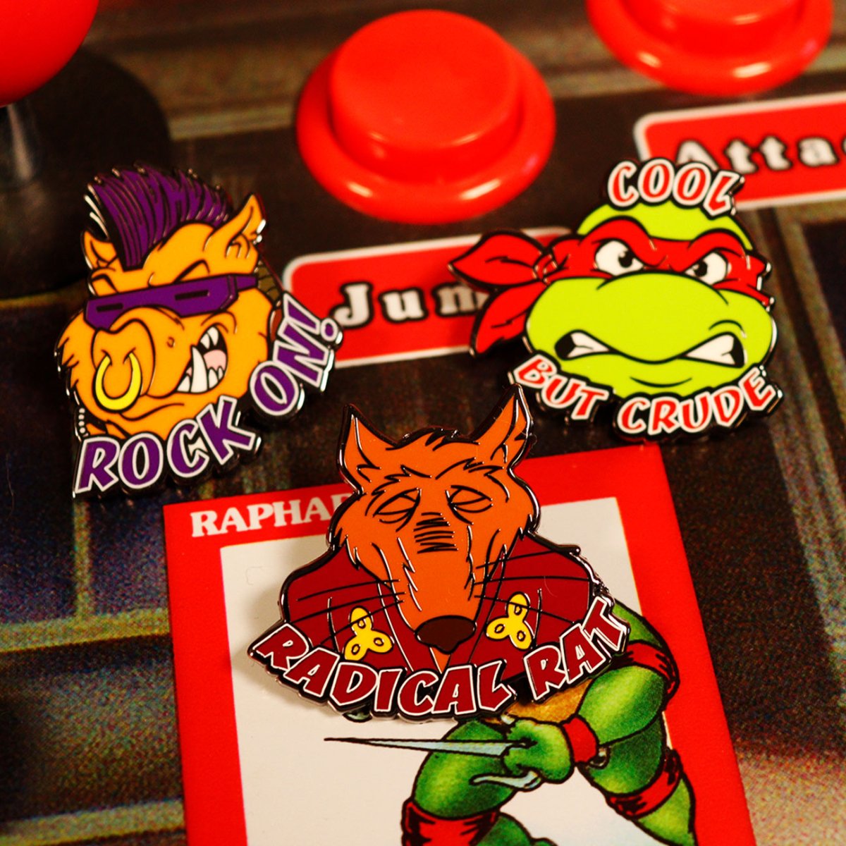 Close-up of the Bebop, Raphael and Splinter TMNT enamel pins displayed on a retro arcade control panel