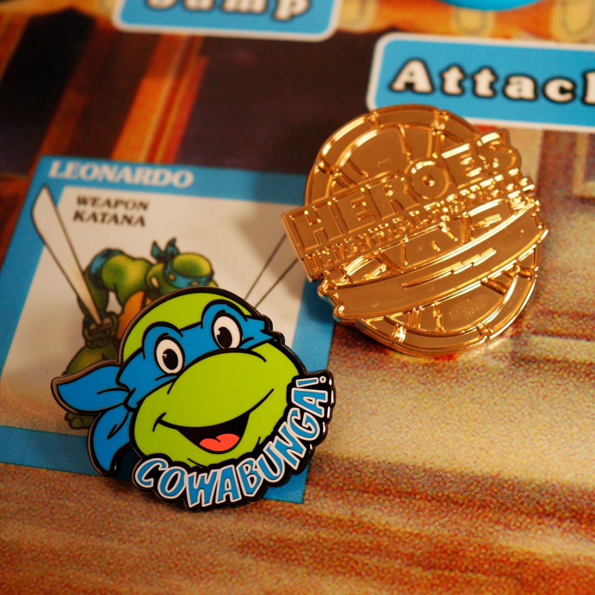 Leonardo Cowabunga TMNT enamel pin beside the rare gold Heroes in a Half Shell pin badge