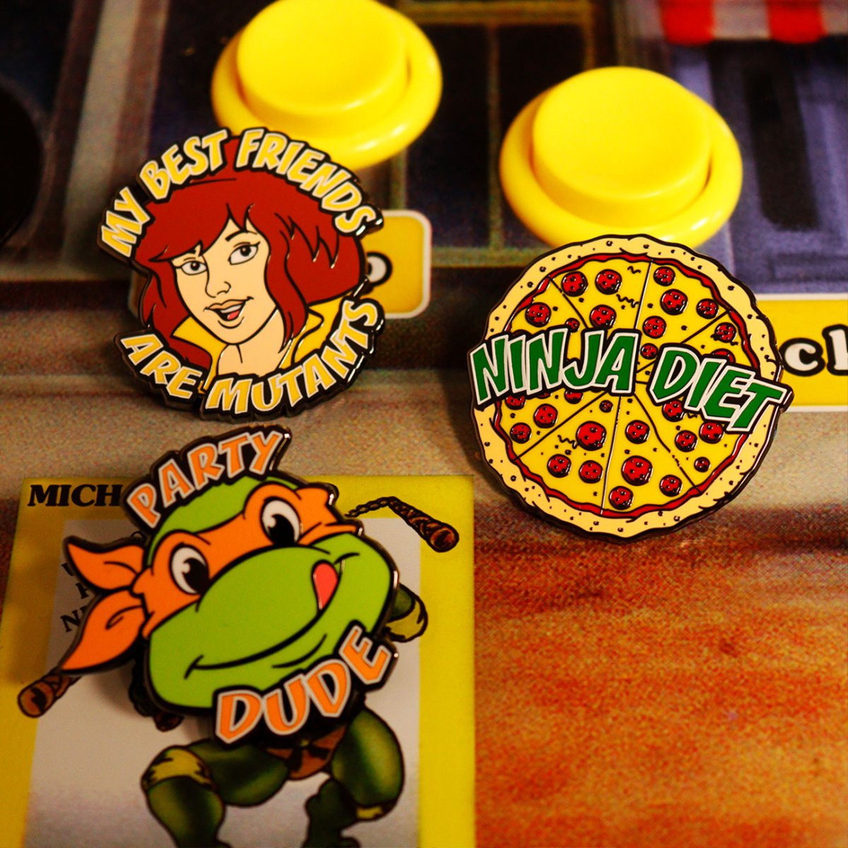 TMNT enamel pins of April, a Ninja Diet pizza and Michelangelo Party Dude on a retro arcade panel