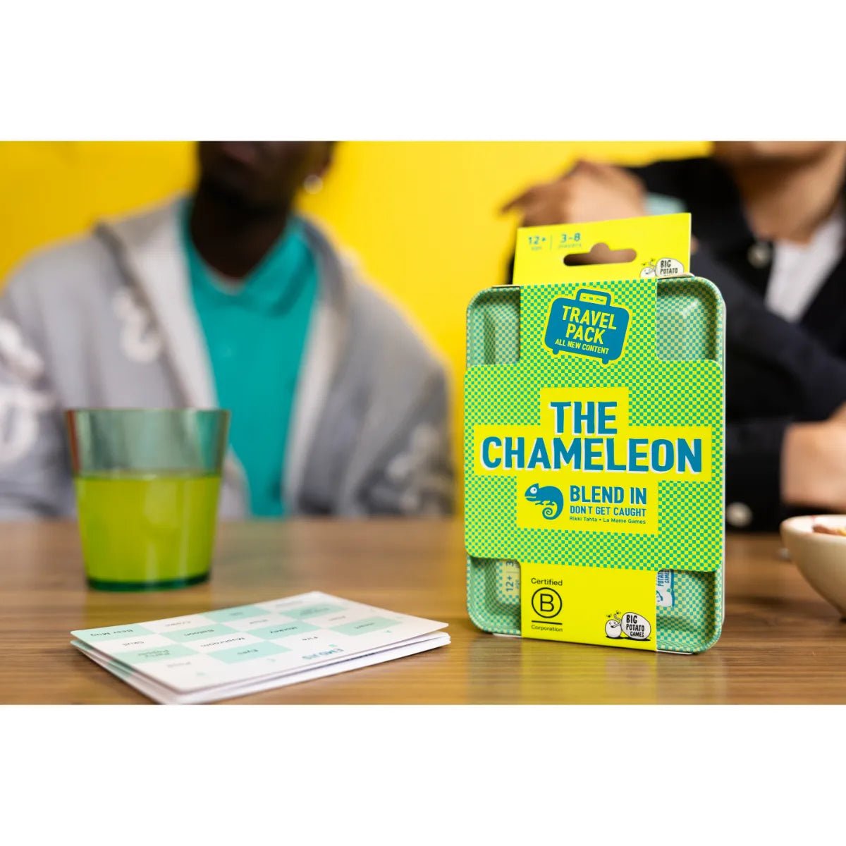 The Chameleon Travel tin on a table beside topic cards and a drink