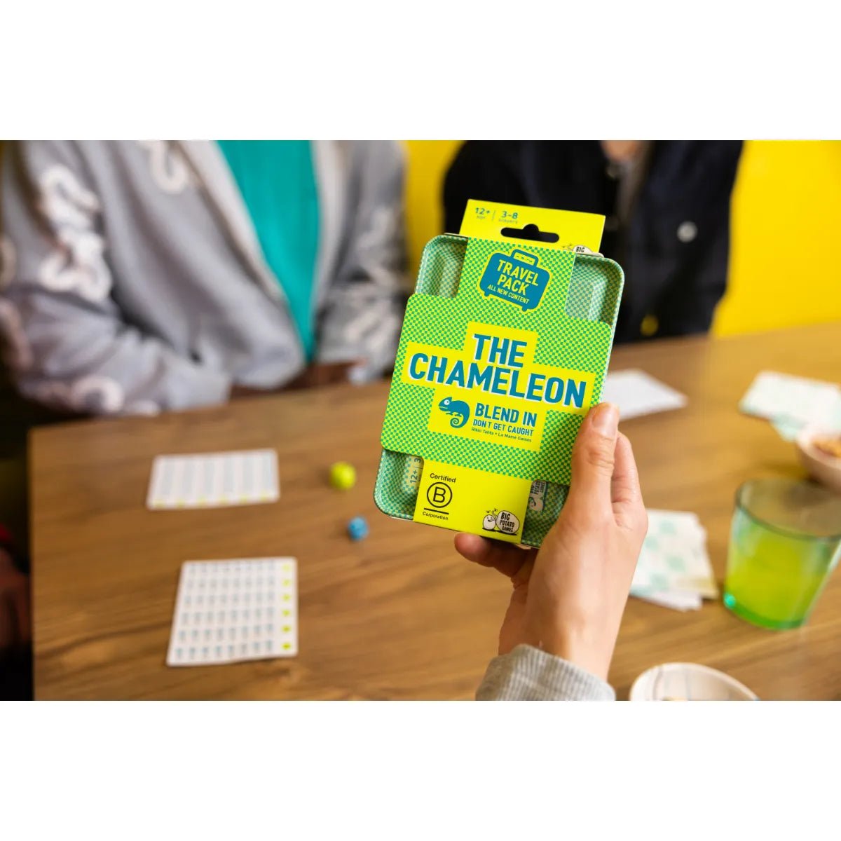 Player holding The Chameleon Travel tin above a table with cards and dice