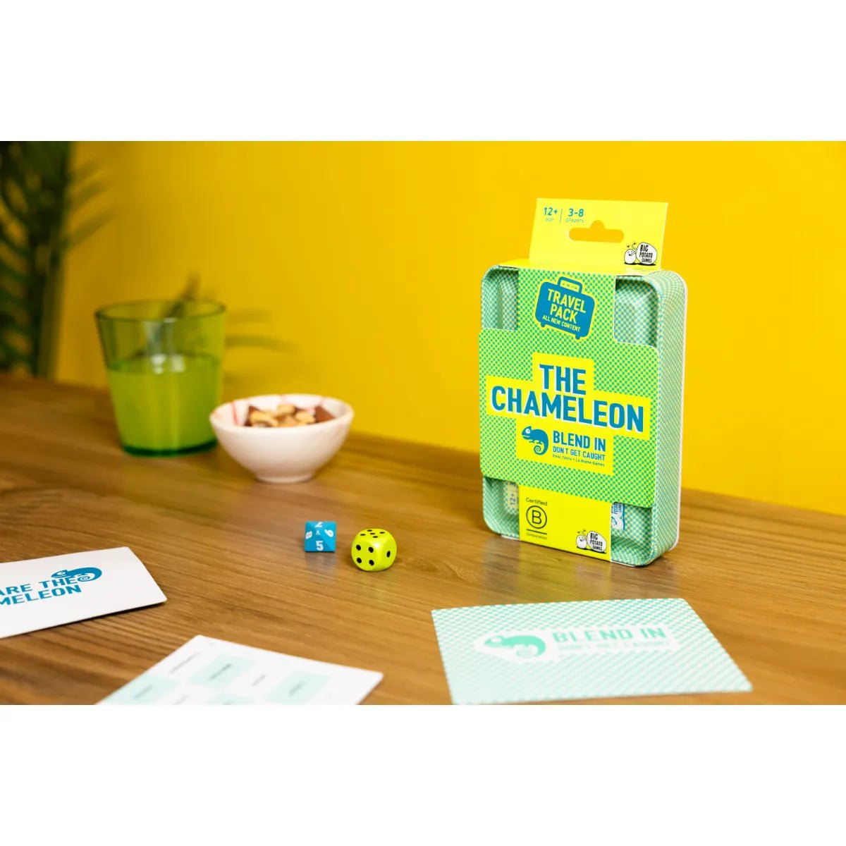 The Chameleon Travel tin standing on a wooden table with dice, cards and snacks
