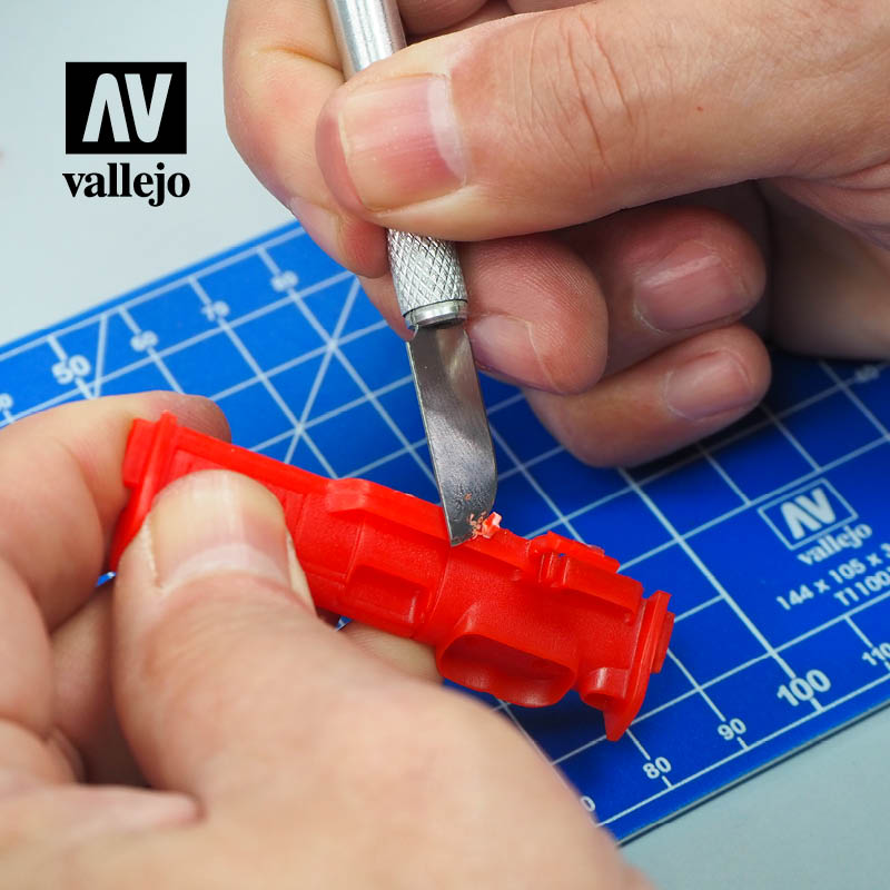 Trimming a red plastic part with a Vallejo hobby knife blade over a cutting mat