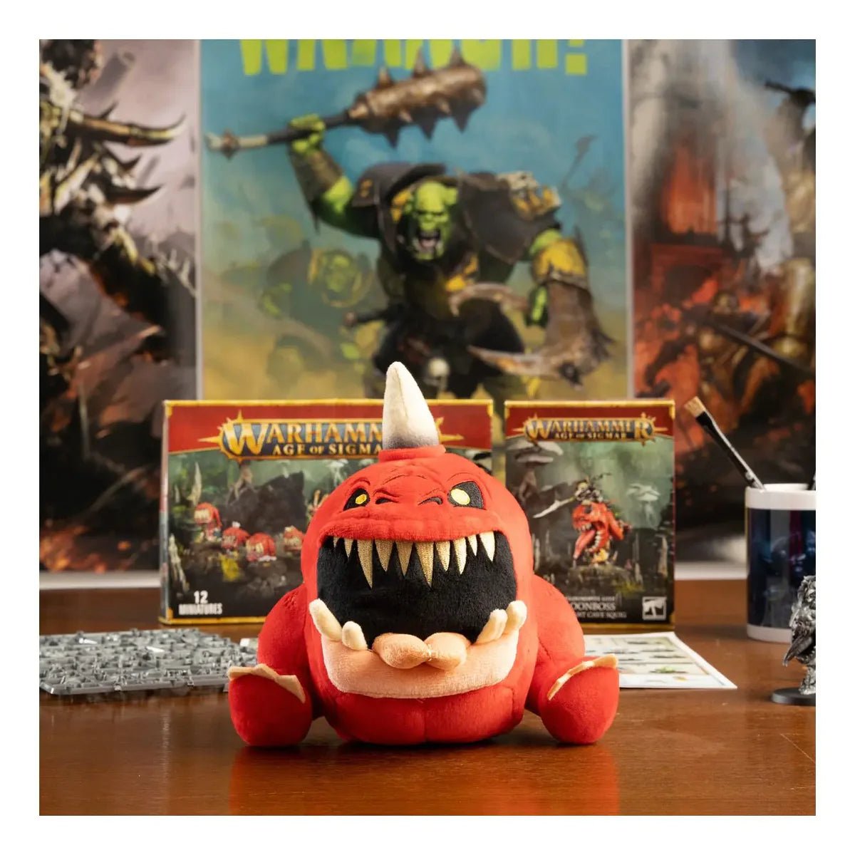 Gnasha-Squig plush on a desk in front of Warhammer Age of Sigmar boxes and Orruk artwork