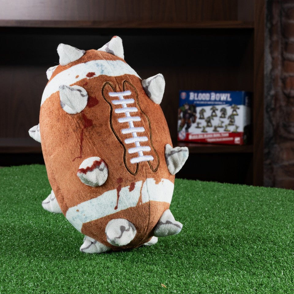TOMY Blood Bowl ball plush standing on green turf in front of a Blood Bowl game box