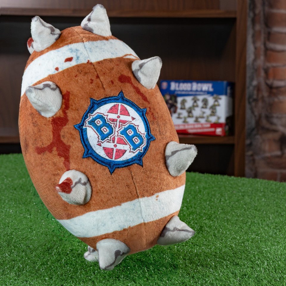TOMY Blood Bowl ball plush on green turf showing the BB logo side