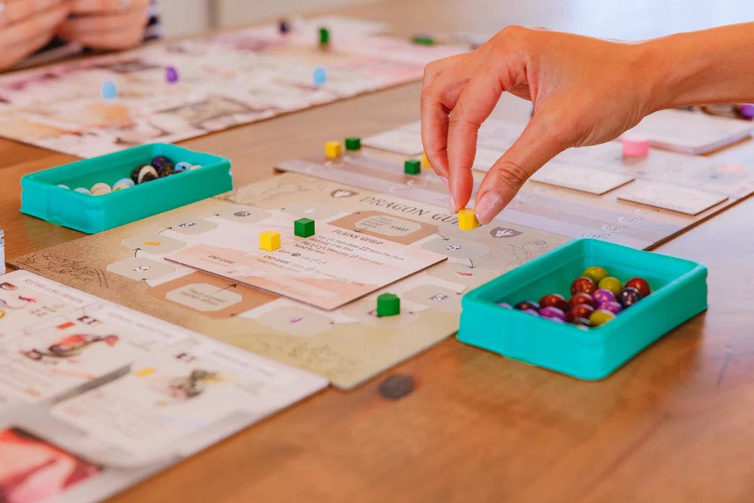 Player placing a coin in a Wyrmspan game, with egg tokens in teal trays