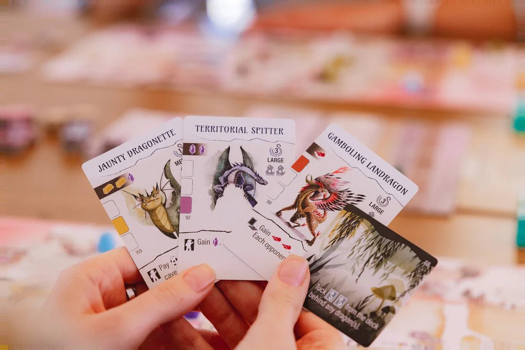 Hand of three illustrated Wyrmspan dragon cards held over the table